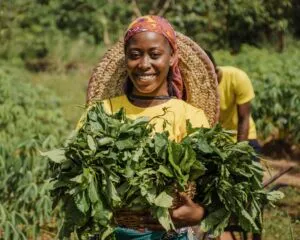 A woman holding a bundle of leafy crops in a cultivated field.